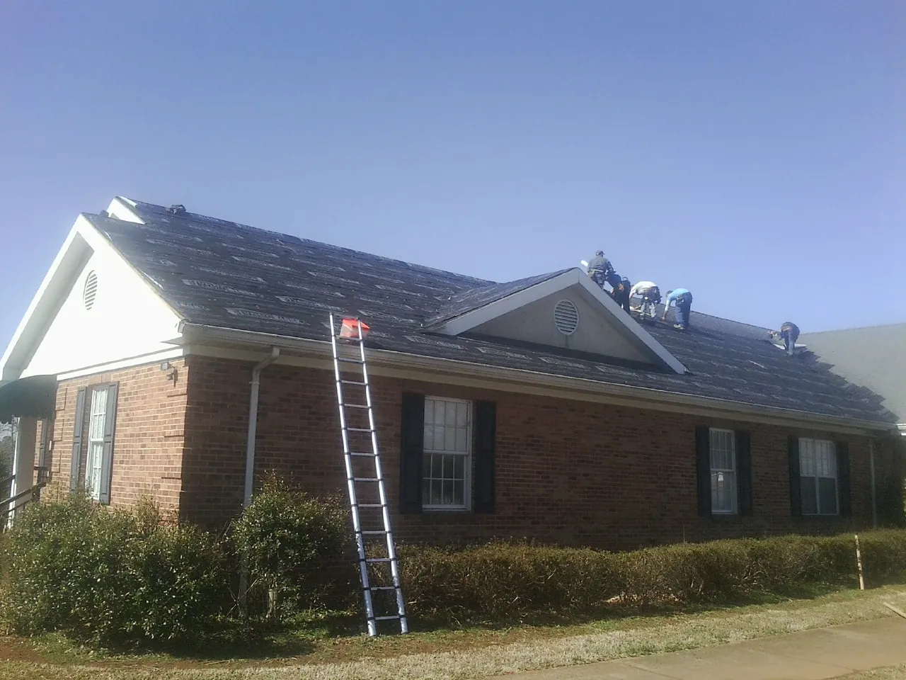 Crew tearing shingles off a brick ranch roof with a ladder set — Metal Roof Repair work by our crew in Aaronsburg