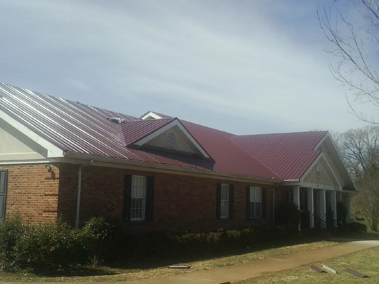 Red metal roof with gabled entries on a long brick building, from a Hail Damage Roof Repair job in Aaronsburg