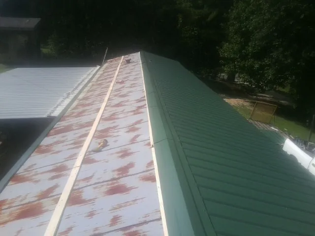 Old rusted panels beside newly installed green metal roofing — Wind Damage Roof Repair by Roofing Brothers in Aaronsburg