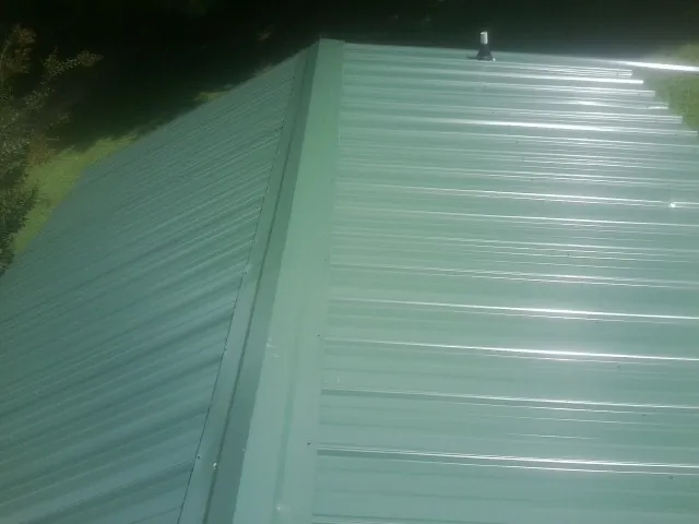 New green metal panels meeting at the ridge of a roof — Flat Roof Repair work by our crew in Aaronsburg