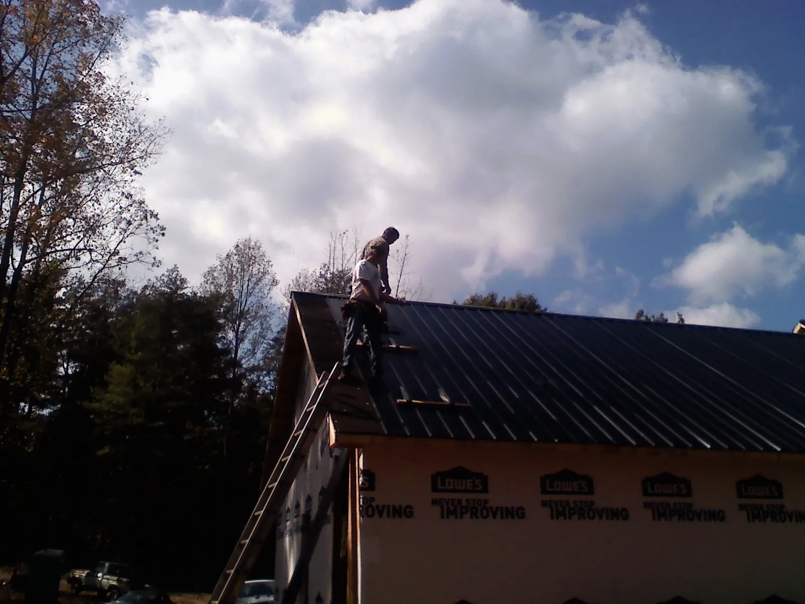 Roofer fastening dark metal panels high against a cloudy sky, from a Roof Inspection job in Aaronsburg