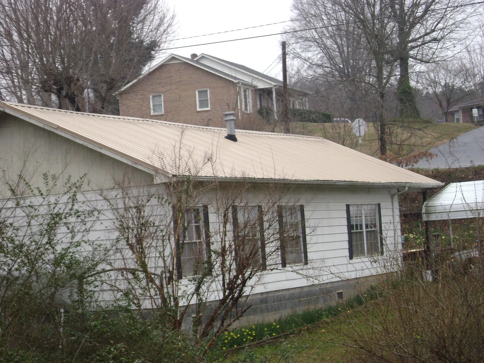Tan metal roof on a white sided house set into a hillside — Commercial Roofing by Roofing Brothers in Aaronsburg